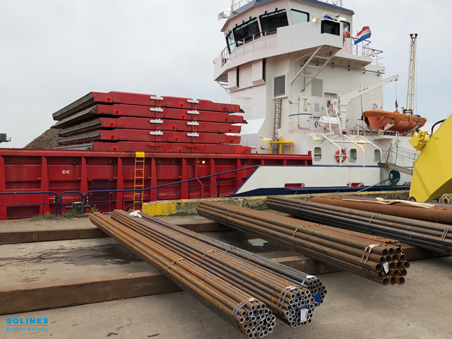 Stalen_buizen_liggen_op_de_kade_in_de_haven_van_Rotterdam-met-boot